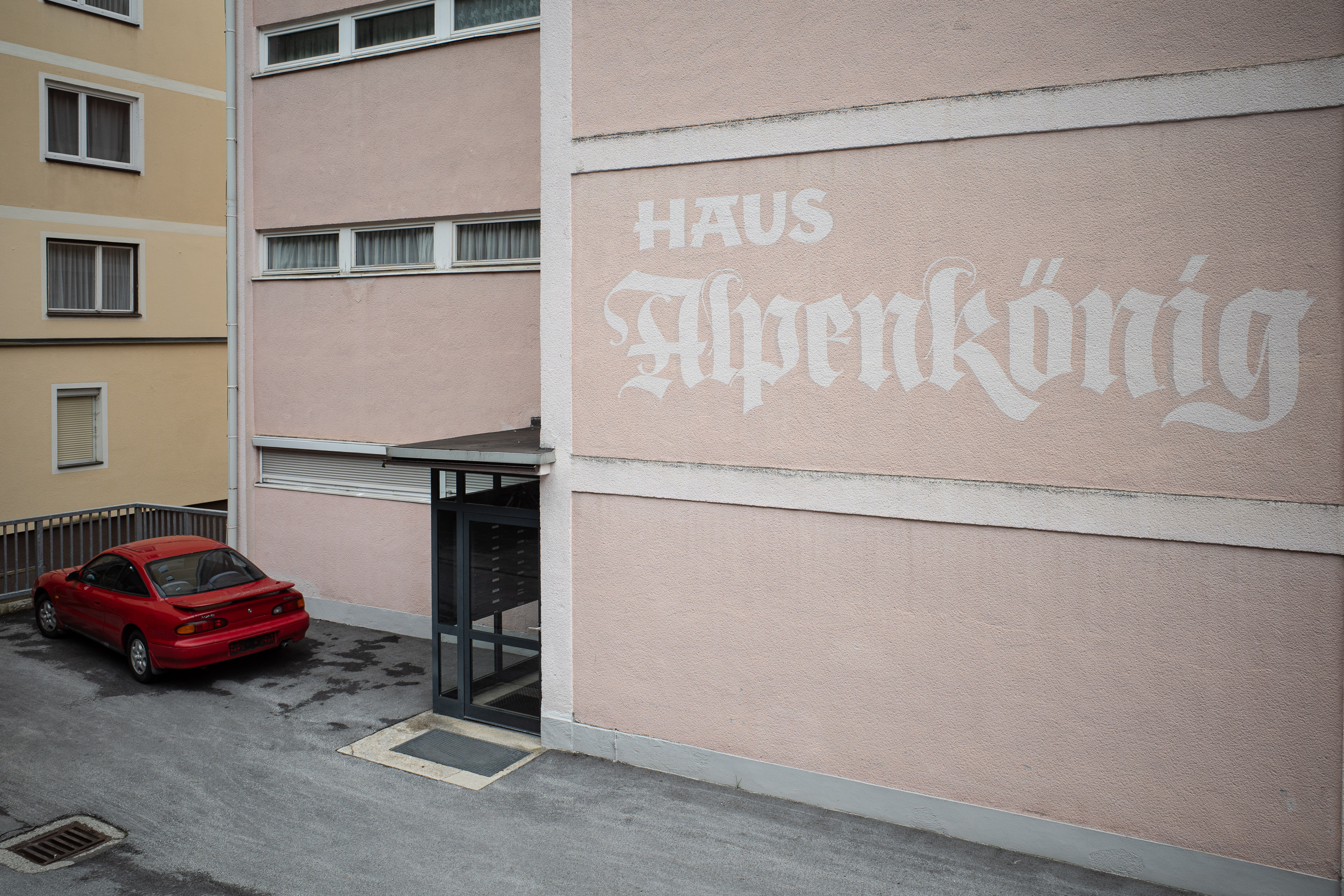 Haus Alpenkönig: Frakturschrift auf rosa Putz, davor ein roter Coupé